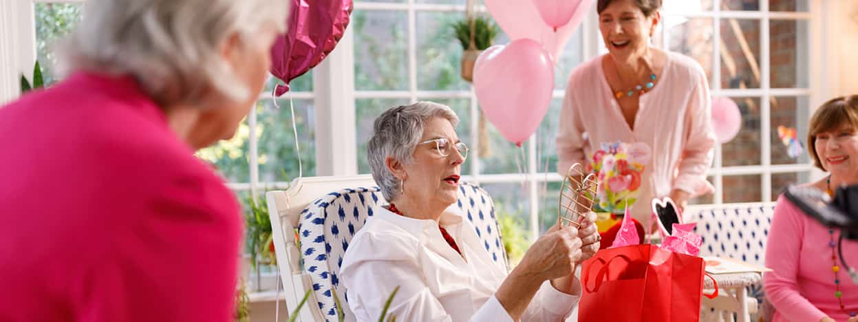 Older woman opening a gift with friends in background